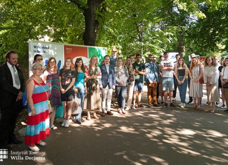 fotografia. wystawa Wyszehrad to ludzie na krakowskich plantach. autorzy wystawy pozują do zdjęcia obok plakatów ustawionych w rzędzie.